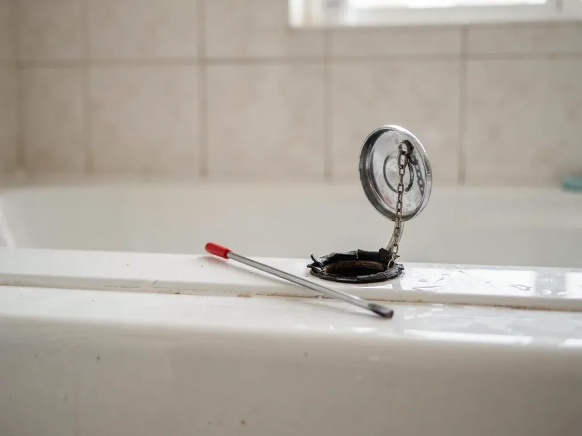 Bathtub overflow plate removed to reveal the hardened perished gasket behind it, the usual source of a tub leak
