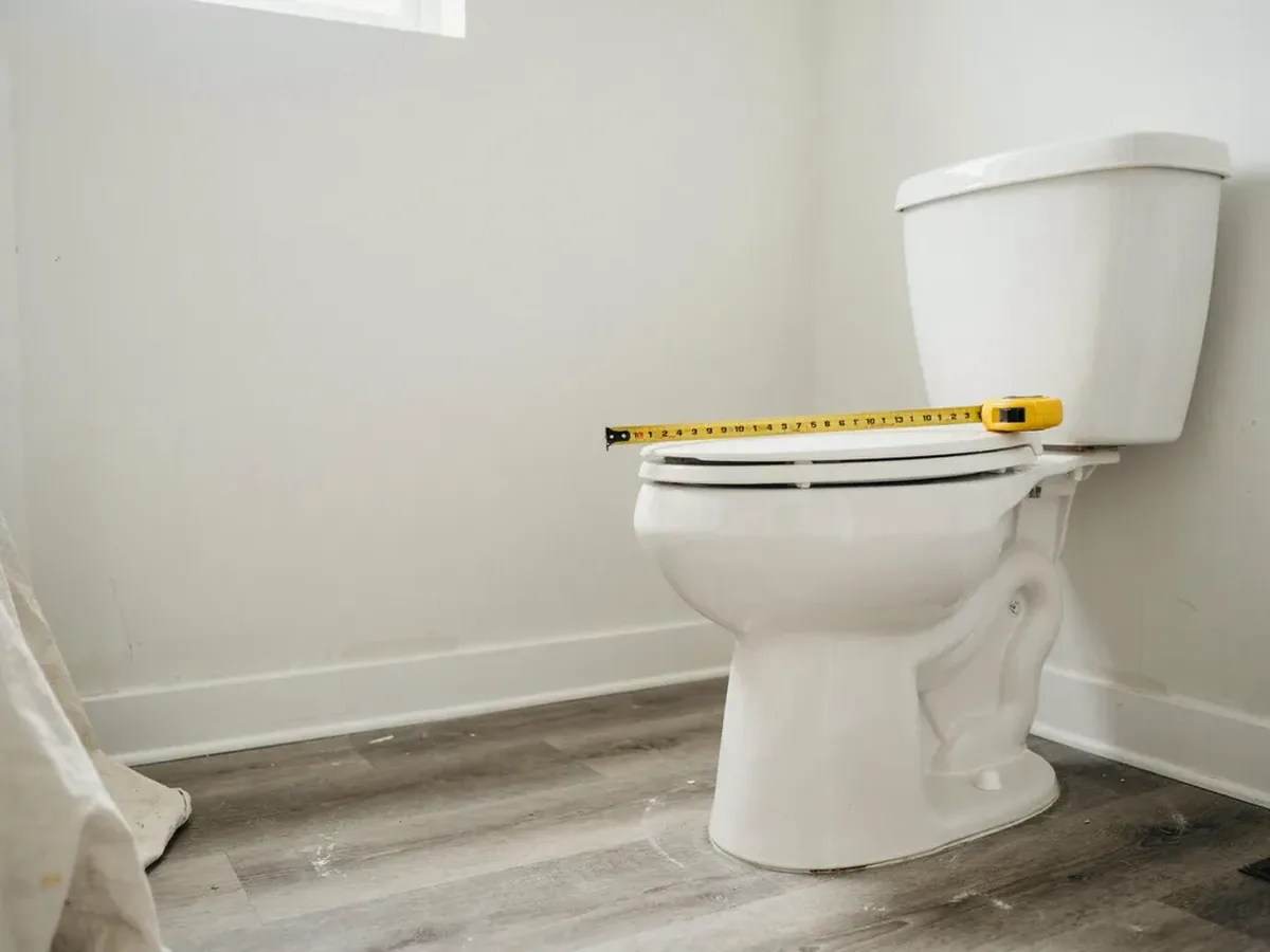 Bathroom with no electrical outlet near the toilet and a tape measure laid across the bowl to check its length