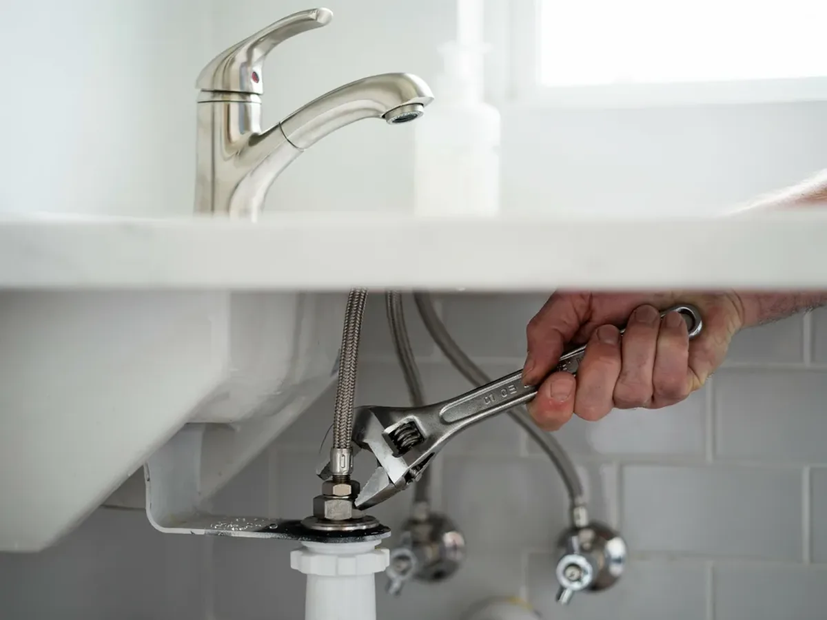 Plumber installing a brushed nickel faucet on a bathroom vanity with new supply lines and shutoff valves
