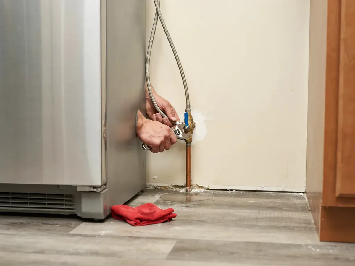 Refrigerator pulled away from the wall exposing a braided water supply line and quarter-turn shutoff valve