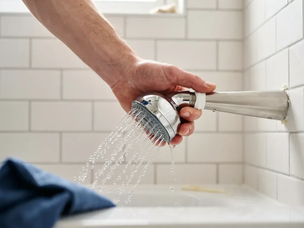 Plumber fitting a chrome shower head onto a new shower arm with water beginning to spray
