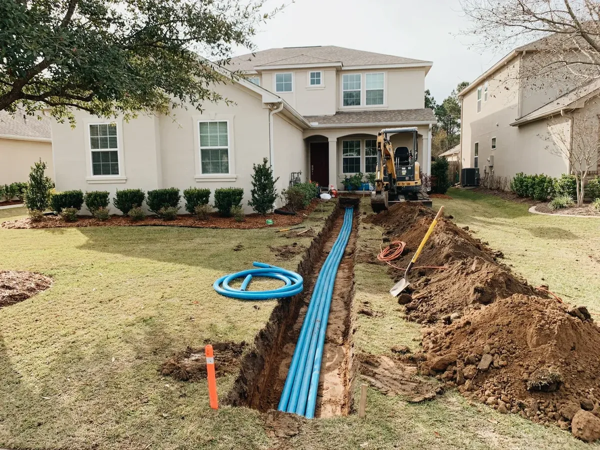 Open trench across a suburban front yard with a new blue polyethylene water service pipe laid into it
