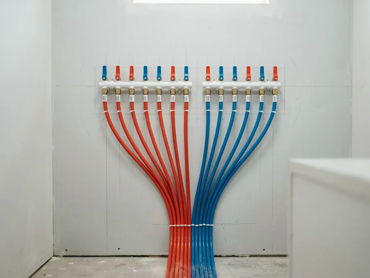 Plumbing manifold with red and blue PEX lines fanning out to a row of labelled shutoff valves